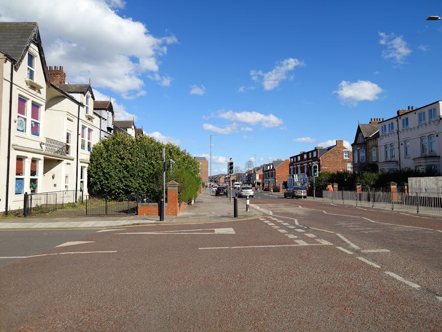 A view of a residential street in West Brompton with a clear blue sky and scattered clouds. On the left, there are white and cream Victorian-style houses with bay windows, some featuring small balconi