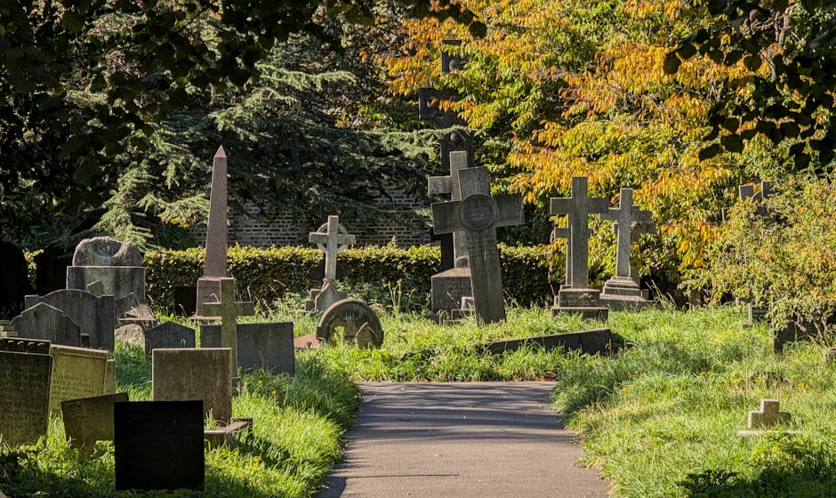 A photograph of a collection of old gravestones and crosses within a cemetery, partially obscured by dense greenery and bushes. The gravestones are made of stone and vary in height and design, with so
